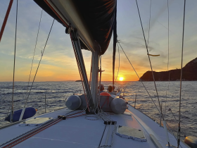 A stunning sunset view from the deck of a sailboat, with guests enjoying the serene ocean scenery — perfect for romantic evenings or sunset cruises.
