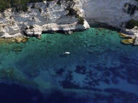 A stunning aerial view of a boat navigating through crystal-clear turquoise waters along a picturesque coastline, showcasing the beauty of nature and adventure on the water.