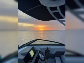 A serene view from the helm of a boat, showcasing a stunning sunset over calm waters — perfect for evening cruises.