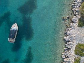 Aerial view of a boat cruising in crystal-clear waters, showcasing the stunning coastline and rocky shore — perfect for exploring secluded beaches.