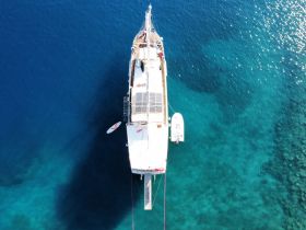 A stunning aerial view of a yacht cruising over crystal-clear waters, showcasing its sleek design and solar panels — perfect for eco-friendly adventures.