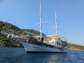 A beautiful side view of the yacht 'Şener Kaptan' docked in tranquil waters, surrounded by lush greenery — perfect for exploring coastal destinations.