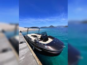A sleek speedboat docked at a picturesque location, showcasing its elegant design against a backdrop of clear turquoise waters and a sunny sky.