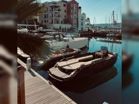 A sleek boat named 'Celestial Charter' docked at a marina, surrounded by other vessels and picturesque buildings, perfect for luxury charters and waterfront views.