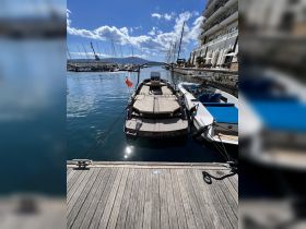 A sleek yacht named 'Molinete' docked at a marina, surrounded by other vessels and a picturesque waterfront view.