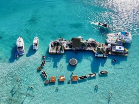 Aerial view of a vibrant beach scene with multiple boats and people enjoying the clear turquoise waters — a perfect destination for water activities and relaxation.