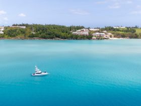 A stunning aerial view of a yacht cruising through the vibrant turquoise waters, with a picturesque coastal landscape in the background — perfect for showcasing luxury boating experiences.
