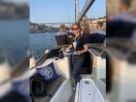 A crew member serves drinks aboard a sailboat, creating a festive atmosphere as guests enjoy the scenic views along the waterfront.