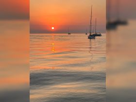 Sailboats glide across the water at sunset, creating a picturesque scene perfect for romantic evenings or sunset cruises.