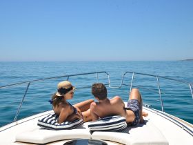 A couple enjoys a relaxing moment on the bow of a boat, soaking up the sun and the serene ocean views — perfect for romantic getaways or leisurely days on the water.