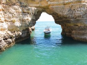 A boat navigates through a stunning natural arch along the coastline, showcasing the beauty of marine exploration and adventure.