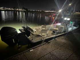 A sleek speedboat docked at night, illuminated by surrounding lights, showcasing its fishing gear and spacious layout — perfect for nighttime adventures on the water.