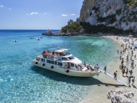 A lively scene at a picturesque beach with a boat anchored nearby, where guests enjoy swimming and sunbathing — a perfect getaway for beach lovers.