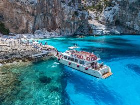 A vibrant scene of a boat anchored near a beautiful beach, with groups of people enjoying the sun and water — a perfect destination for a fun-filled day on the water.