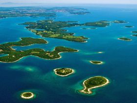 A stunning aerial view of a cluster of lush green islands surrounded by vibrant turquoise waters, showcasing the natural beauty of the coastline.