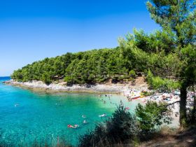 A vibrant beach scene with groups of people enjoying the clear turquoise waters and sunbathing along the coastline — a perfect summer getaway.