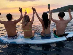 A group of friends celebrates at sunset while paddleboarding, capturing the joy of summer adventures on the water.