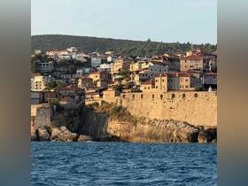A picturesque view of a coastal town with charming stone houses and a historic fortress, set against a backdrop of lush hills — a perfect representation of scenic waterfront destinations.