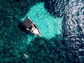 An aerial view captures a swimmer enjoying the crystal-clear waters beside a sleek boat, showcasing the perfect day for water activities and exploration.