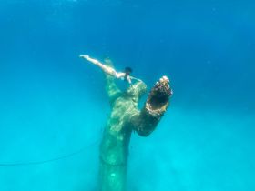 A swimmer explores an underwater sculpture, showcasing the beauty of marine life and adventure in crystal-clear waters.