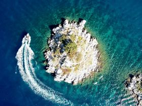 A stunning aerial view of a small island surrounded by crystal-clear waters, with a boat creating a wake as it navigates the vibrant sea — perfect for showcasing the beauty of marine adventures.