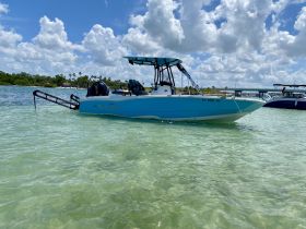 A NauticStar boat anchored in clear waters, showcasing its sleek design against a backdrop of fluffy clouds and lush greenery.