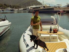 A man enjoys a celebratory moment on a boat with champagne and a dog by his side, set against a picturesque marina backdrop.
