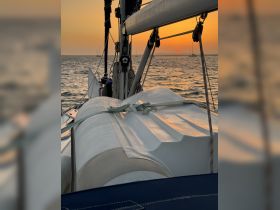 A serene sunset view from the deck of a sailboat, showcasing the vessel's structure against the backdrop of a beautiful horizon.