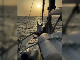 A serene view of a sailboat at sunset, showcasing the vessel's structure against the shimmering water — perfect for tranquil sailing experiences.