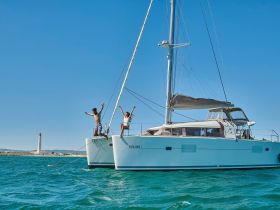 A couple joyfully celebrates aboard a catamaran, with a picturesque lighthouse in the background — perfect for sailing adventures and memorable moments on the water.
