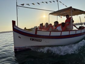 A lively group enjoys a boat ride at sunset, wearing life jackets and capturing the moment on the water — perfect for adventure seekers and sunset lovers.