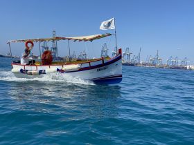 A vibrant boat navigates through the harbor, showcasing the bustling backdrop of shipping cranes and clear blue waters — perfect for exploring coastal areas.