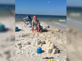 A young girl joyfully builds a sandcastle on the beach, capturing the essence of summer fun and creativity by the shore.