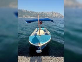 A clear view of a small boat docked by the shore, showcasing its vibrant blue color and canopy against a scenic mountainous backdrop.