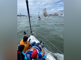 A group of friends relaxes on the deck of a sailboat, enjoying a vibrant sailing experience amidst a fleet of boats, perfect for adventure seekers and sailing enthusiasts.