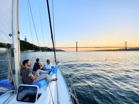 A group enjoys a scenic sunset sail in Lisbon, with the iconic bridge in the background, creating a perfect atmosphere for relaxation and exploration on the water.