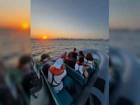 A group of guests enjoys a stunning sunset view from their boat, capturing the moment against a backdrop of a city skyline — perfect for memorable evening cruises.