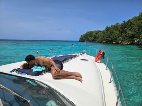 A couple enjoys a moment of relaxation on the deck of a boat, surrounded by stunning turquoise waters and lush greenery — an idyllic tropical getaway.