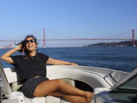 A joyful woman relaxes on a boat with a stunning bridge in the background, capturing the essence of a perfect day on the water.