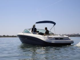 A speedboat glides through calm waters with two people onboard, showcasing a perfect day for boating adventures.