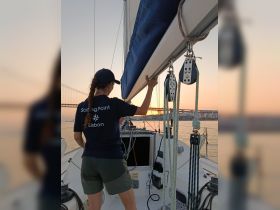 A sailor adjusts the sail on a boat during a beautiful sunset in Lisbon, capturing the essence of an adventurous sailing experience.