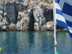 A scenic view of rocky cliffs reflected in calm waters, with a flag in the foreground. The image lacks clarity and detail.