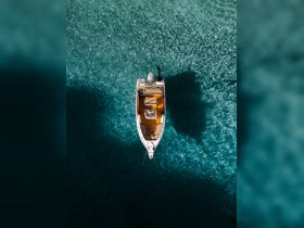 A stunning aerial view of a boat gliding over crystal-clear waters, showcasing the vessel's sleek design and inviting deck — perfect for exploring beautiful coastal destinations.