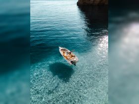 An aerial view of a boat floating gracefully over crystal-clear waters, showcasing the stunning underwater scenery — perfect for exploring coastal destinations.