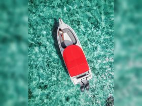 Aerial view of a stylish boat with a red canopy, showcasing a serene moment on turquoise waters — perfect for summer adventures and relaxation.
