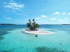 A stunning aerial view of a secluded island surrounded by crystal-clear turquoise waters, showcasing a perfect beach getaway with guests enjoying the serene environment.
