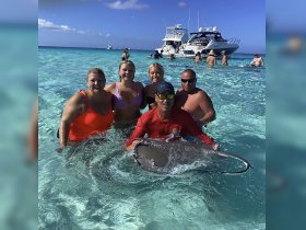 A group of friends interacts with a stingray in shallow waters, creating a memorable wildlife experience in a tropical paradise.