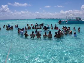 A lively group enjoys a fun day in the shallow turquoise waters, creating unforgettable memories while surrounded by friends and a boat in the background.