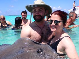 A couple interacts with a stingray while enjoying a swim in crystal-clear waters, showcasing a memorable wildlife experience in the Bahamas.