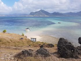 A stunning view of a boat anchored near a sandy beach, surrounded by turquoise waters and picturesque mountains — an ideal destination for relaxation and exploration.